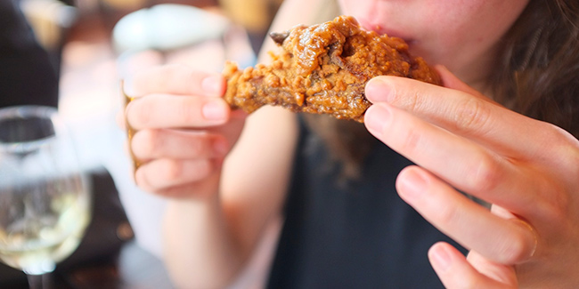 A happy diner bites into a piece of fried chicken